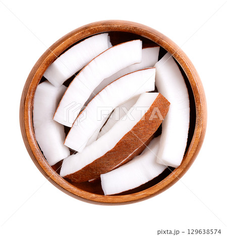 Raw coconut meat, in a wooden bowl. Opaque white flesh of a fresh and young coconut, cut into strips, and ready to eat. Seed of the palm tree Cocos nucifera. Isolated on white background, food photo. 129638574