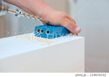 Skilled hands using drilling guide to create precise holes in wooden surface for an efficient woodworking project 129639102