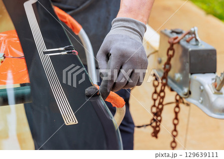 Skilled technician repairing car window with precision tools outdoors during replace windshield Skilled technician repairing car window with precision tools outdoors during replace windshield 129639111