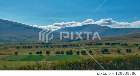 Serene landscape showcases gently rolling hills and distant mountains on a sunny day 129639580