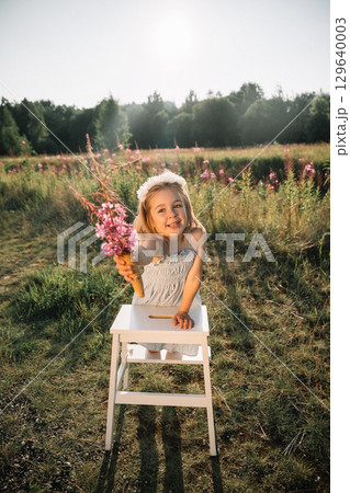 Little girl holding flowers in ice cream cone in a sunlit field with blooming plants during golden 129640003