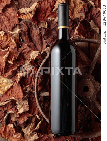 Bottle of red wine and dried-up vine leaves. 129640053