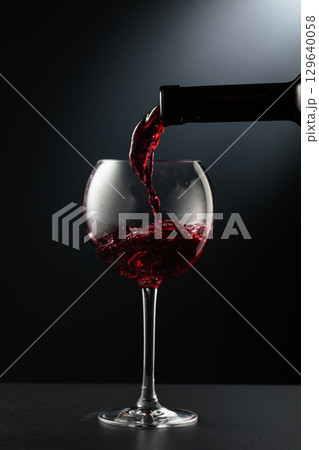 Pouring red wine into a wine glass. 129640058