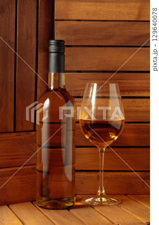 Bottle and glass of white wine on a wooden background. Bottle and glass of white wine on a wooden background. 129640078