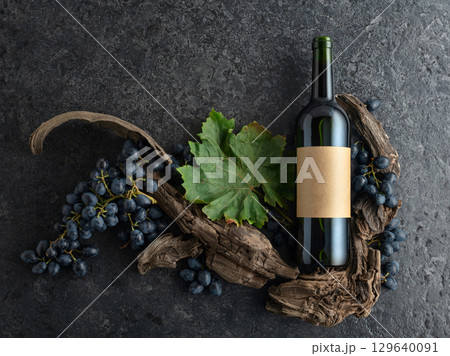 Bottle of red wine, blue grapes, and old vine snags on a black stone background. 129640091