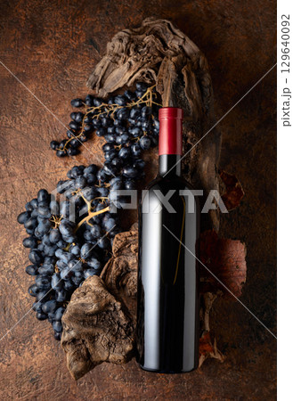 Bottle of red wine with blue grapes and old weathered snags. Bottle of red wine with blue grapes and old weathered snags. 129640092