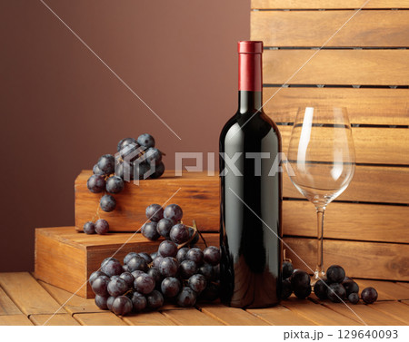 Bottle and glass of red wine and blue grapes on a wooden background. 129640093