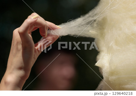 A Close-Up of a Hand Gently Pulling Cotton Candy, Emphasizing the Silky Texture and Lightness of This Sweet Treat at a Fun Fair or Carnival Setting 129640218