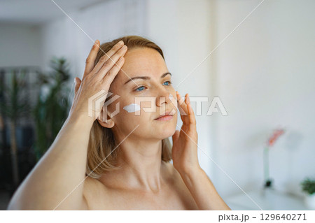 Woman applying face cream at home for her daily skincare routine 129640271