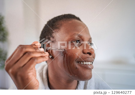 Smiling woman applying serum on face with pipette Smiling woman applying serum on face with pipette 129640277