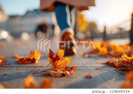 Colorful autumn leaves blanket the sidewalk as a person walks during a sunny afternoon Colorful autumn leaves blanket the sidewalk as a person walks during a sunny afternoon 129640534