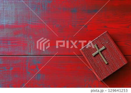 Vintage red-painted wooden bible box with handcrafted cross symbol placed against distressed red wooden planks background featuring weathered blue undertones and natural wood grain patterns. Religious 129641253