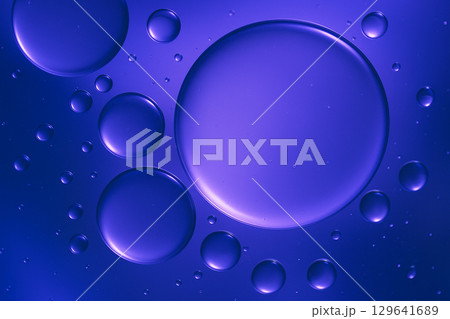 Close-up abstract of large purple oil droplets floating in blue-toned liquid with vibrant glow 129641689