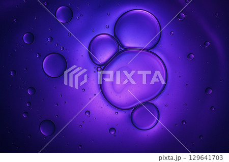 Macro shot of transparent oil bubbles illuminated with purple light floating in liquid 129641703