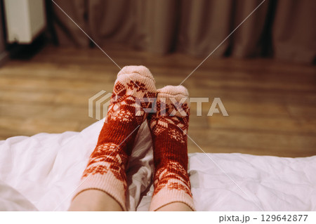 Female feet wearing festive patterned socks, relaxing on bed indoors. Cozy feet resting on sofa, warm, patterned winter socks. Comfort relaxing moment Female feet wearing festive patterned socks, relaxing on bed indoors. Cozy feet resting on sofa, warm, patterned winter socks. Comfort relaxing moment 129642877