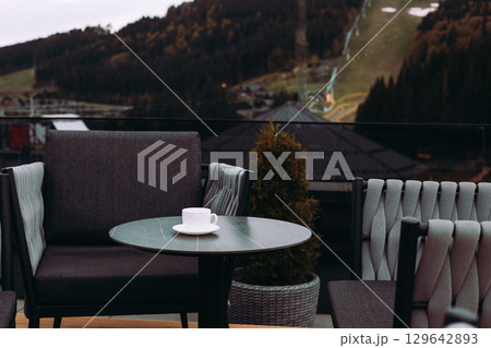 A cup of coffee, tea on a table and scenic mountain view. A tranquil scene of hotel terrace, rooftop with mountain backdrop. Relaxation, leisure scene A cup of coffee, tea on a table and scenic mountain view. A tranquil scene of hotel terrace, rooftop with mountain backdrop. Relaxation, leisure scene 129642893