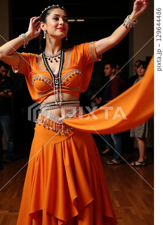 Amidst a buzzing crowd, a dancer adorned in elegant orange costume twirls gracefully, showcasing her talent during a festive celebration filled with rhythm and excitement. 129644486