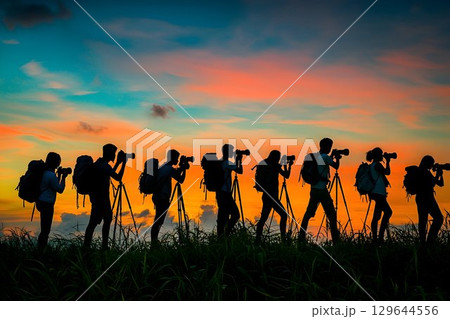Silhouette of photographers capturing sunset with tripods in gra 129644556