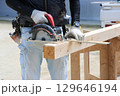 大工さんが丸ノコと丸ノコ用角度切り定規を使って木材を切断している 129646194