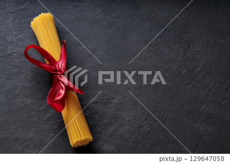 Raw Spaghetti Bundle Tied with Red Ribbon on Dark Background Top View Copy Space 129647058