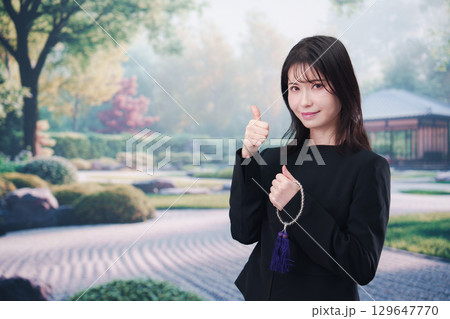 喪服を着て数珠を持って手を合わせる女性 129647770
