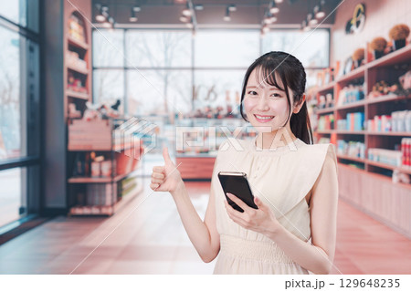 ショッピングをしながらスマホで検索をする若い女性 ショッピングをしながらスマホで検索をする若い女性 129648235