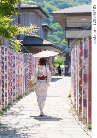 カラフルな友禅ポールが並ぶ「キモノフォレスト」を和服で歩く女性、京都・嵐山 カラフルな友禅ポールが並ぶ「キモノフォレスト」を和服で歩く女性、京都・嵐山 129648485