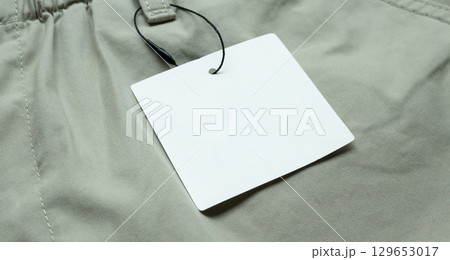 Blank white clothes tag label on gray fabric texture background 129653017