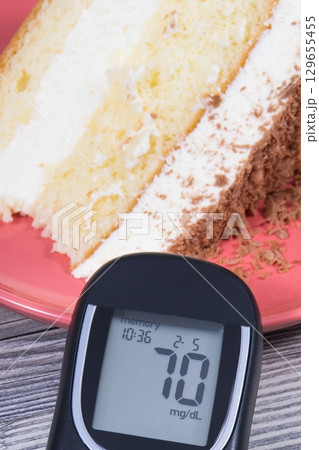 Glucose meter with result of sugar level and cake with layers and chocolate 129655455