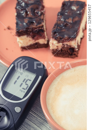 Glucose meter with result of sugar level, cheesecake with cherries and chocolate, coffee with milk 129655457