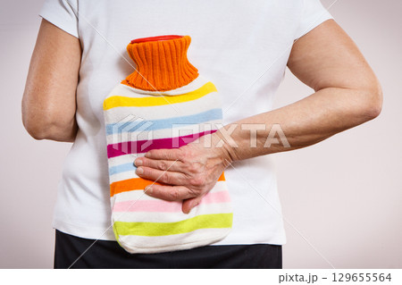 Senior woman with hot water bottle on her back. Help with pain in old age 129655564