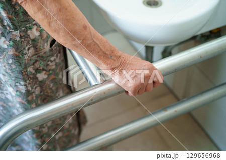 Asian elderly woman patient use toilet support rail in bathroom. 129656968