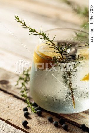 Alcohol drink (gin tonic cocktail) with lemon, juniper branch, and ice on rustic wooden table. 129657078