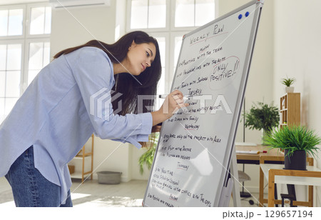 Young attractive woman writing weekly plan holding marker, handwriting Young attractive woman writing weekly plan holding marker, handwriting 129657194