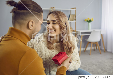 Happy, beautiful, loving, young couple at home in romantic atmosphere celebrate Valentine's Day, man congratulates woman, gives gifts. 129657447