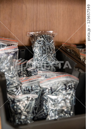 Plastic bags filled with shiny metal screws stored in a black container, organized for construction, repair, and DIY hardware projects. 129657549