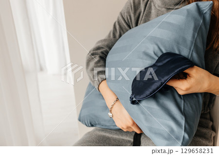 Woman holding blue pillow with matching sleep mask, cozy home comfort concept 129658231