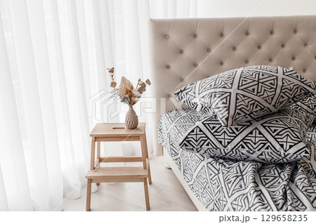 Modern geometric black and white bedding with stacked pillows in bright bedroom interior 129658235