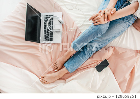 Relaxed remote work setup with laptop, headphones, and smartphone on bed Relaxed remote work setup with laptop, headphones, and smartphone on bed 129658251
