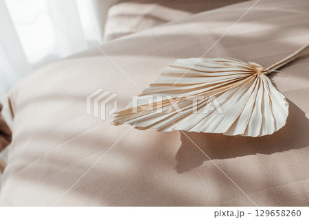 Dried palm leaf decor on beige bed linen in soft sunlight Dried palm leaf decor on beige bed linen in soft sunlight 129658260