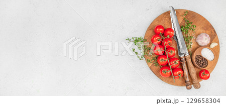 Fresh cherry tomatoes, herbs, and spices arranged on a rustic wooden cutting board for cooking preparation. top view. copy space. 129658304
