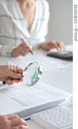 Group of accountants are working together, using a magnifying glass and a calculator, to audit financial reports in office. Audit and taxes in business 129658456
