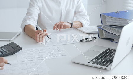 Two accountants collaborating in a well lit office, analyzing financial data and preparing reports with calculators and pens. Audit and taxes in business 129658800