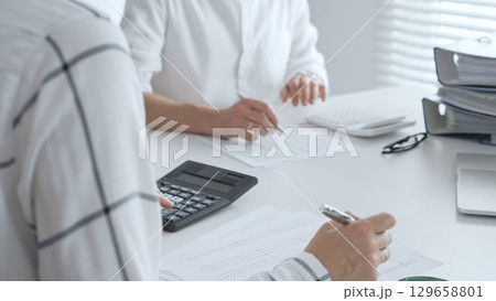 Unrecognizable accountants working together in a well lit office, analyzing financial data and preparing reports with calculators and pens. Audit and taxes in business Unrecognizable accountants working together in a well lit office, analyzing financial data and preparing reports with calculators and pens. Audit and taxes in business 129658801