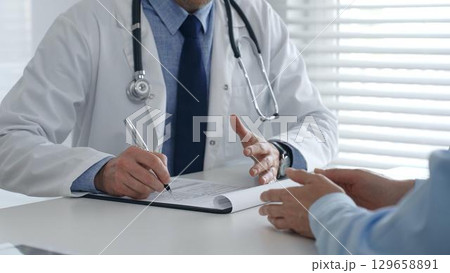 Medical professional documenting patient consultation, writing clinical notes on clipboard during healthcare interaction in professional medical setting. Medicine and health care concept Medical professional documenting patient consultation, writing clinical notes on clipboard during healthcare interaction in professional medical setting. Medicine and health care concept 129658891