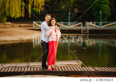 man and pregnant woman in red dress at sunset on the pier  129659824