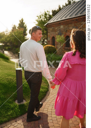 pregnant brunette woman in pink dress holding man's hand and following him. 129659832