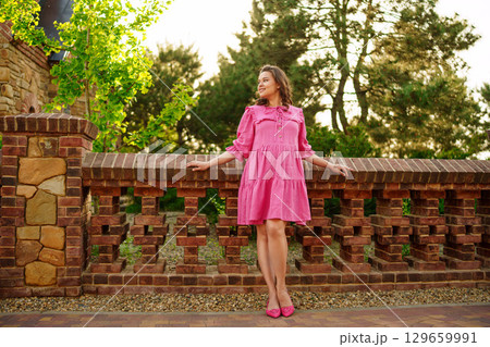 happy pregnant young woman in pink dress by the stone fence 129659991