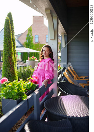 Beautiful young pregnant woman in pink dress on summer veranda.  129660018