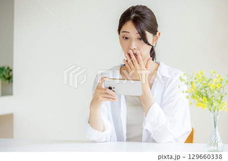 スマホを見て驚く女性 129660338